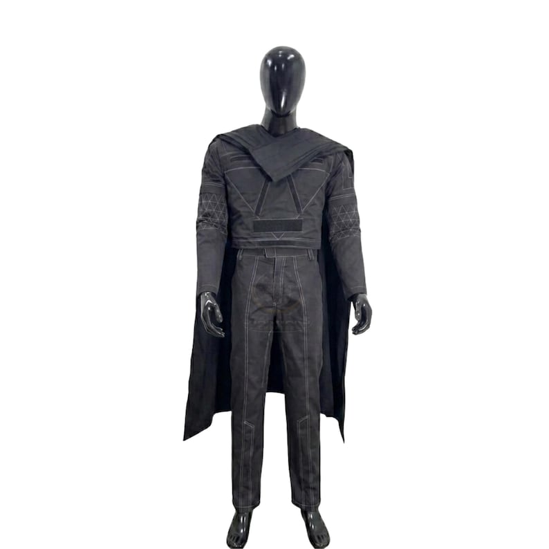 May include: A black costume set on a mannequin, featuring a long-sleeved top with geometric patterns on the sleeves, a matching pair of trousers with visible white stitching, and a long cape draped over the shoulders, all in a dark charcoal black.