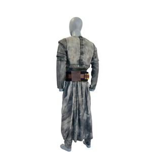 May include: A gray costume with a jacket, long skirt, and belt. The jacket has shoulder pads and long sleeves. The skirt is long and flowing. The belt is brown with gold-colored details. The costume is displayed on a mannequin.