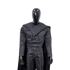 May include: A black costume set featuring a long-sleeved top with a structured collar, a matching cape, and trousers. The garment includes white geometric stitching patterns on the sleeves and white contrast stitching throughout the entire outfit.