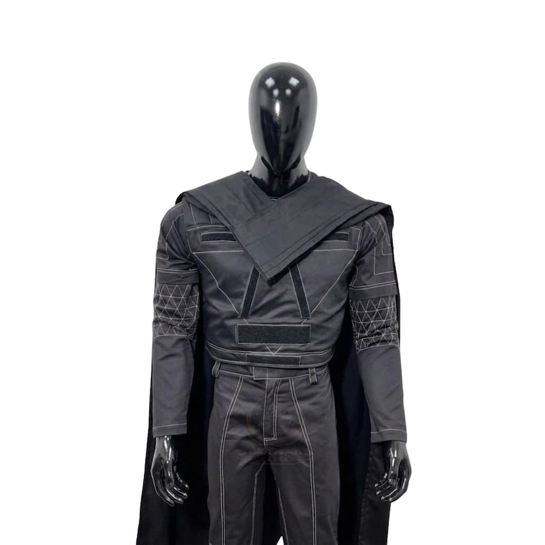 May include: A black costume set featuring a long-sleeved top with a structured collar, a matching cape, and trousers. The garment includes white geometric stitching patterns on the sleeves and white contrast stitching throughout the entire outfit.