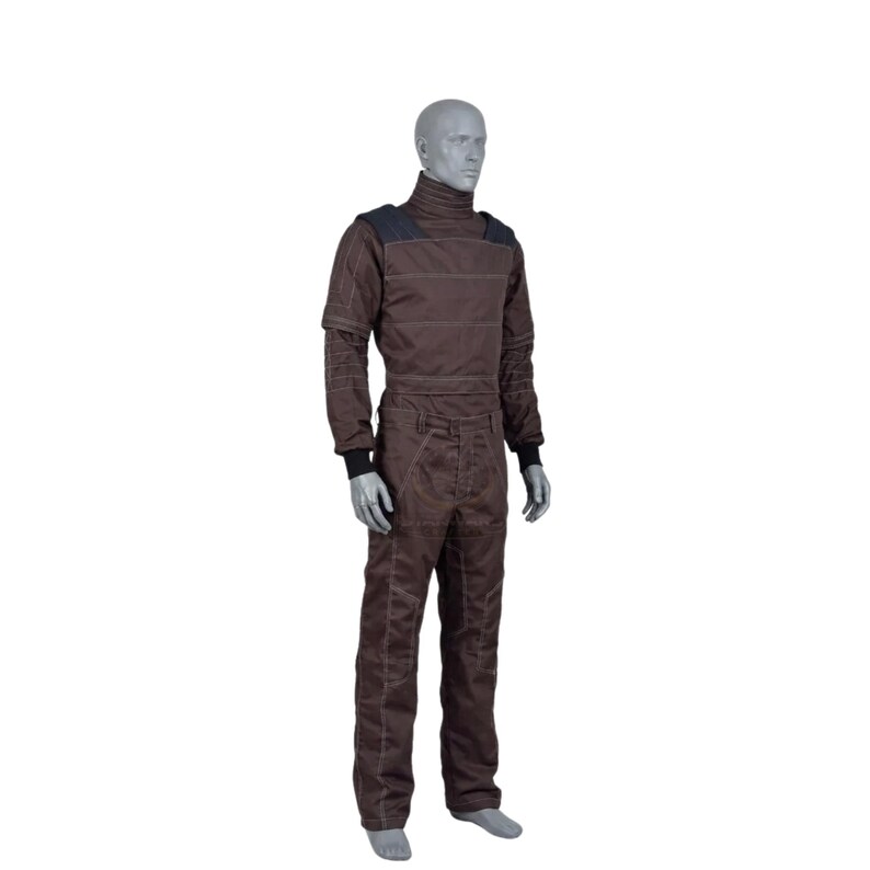 May include: Brown jumpsuit with a high collar and contrasting stitching. The one-piece garment features long sleeves, a zip-up front, and a fitted silhouette. Black cuffs and shoulder accents add detail to the workwear-inspired design.