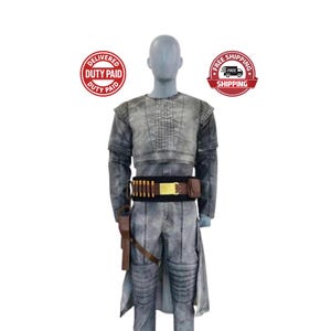 May include: A gray costume with a weathered appearance, featuring a cropped top, long sleeves, and matching pants. A brown belt with bullet casings and a holster with a toy gun are included. The costume is displayed on a mannequin.