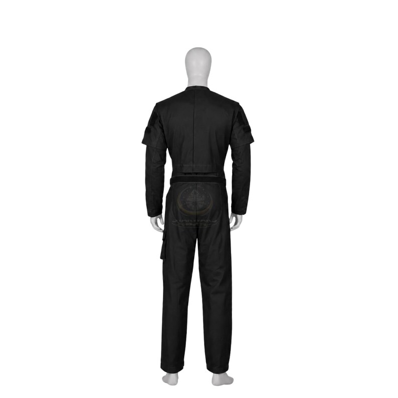 Pode incluir: Um macac&atilde;o t&aacute;tico preto num manequim, com mangas compridas, gola alta e cintura ajustada. A pe&ccedil;a inclui um bolso utilit&aacute;rio na perna direita e um emblema circular estampado na parte de tr&aacute;s das cal&ccedil;as com um design detalhado.