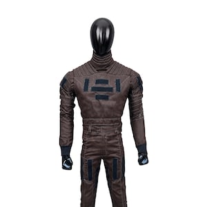 May include: A dark brown long-sleeved jumpsuit featuring a high ribbed collar, padded shoulder detailing, and black rectangular patches on the chest and thighs. The garment includes fitted cuffs and structured stitching throughout the torso and legs.