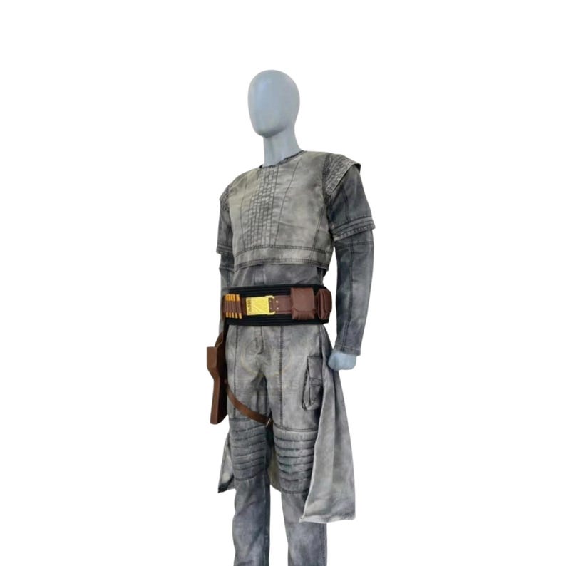 May include: A gray costume with a long-sleeved top, pants, and a belt with gold accents. The costume includes a holster and a draped fabric piece. The outfit is displayed on a mannequin.
