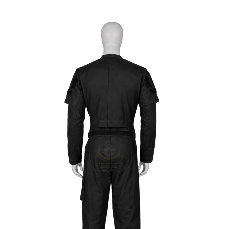 Pode incluir: Um macac&atilde;o t&aacute;tico preto num manequim, com mangas compridas com emblemas nos ombros, cintura ajustada com uma faixa tipo cinto e bolsos cargo nas pernas. A pe&ccedil;a &eacute; de cor preta s&oacute;lida com costuras vis&iacute;veis e tecido estruturado.