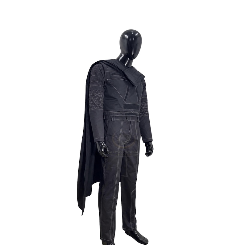 May include: A black costume set displayed on a mannequin, featuring a long cape, a long-sleeved top with geometric white stitching patterns on the sleeves and chest, and matching trousers with visible white seam detailing throughout the garment.