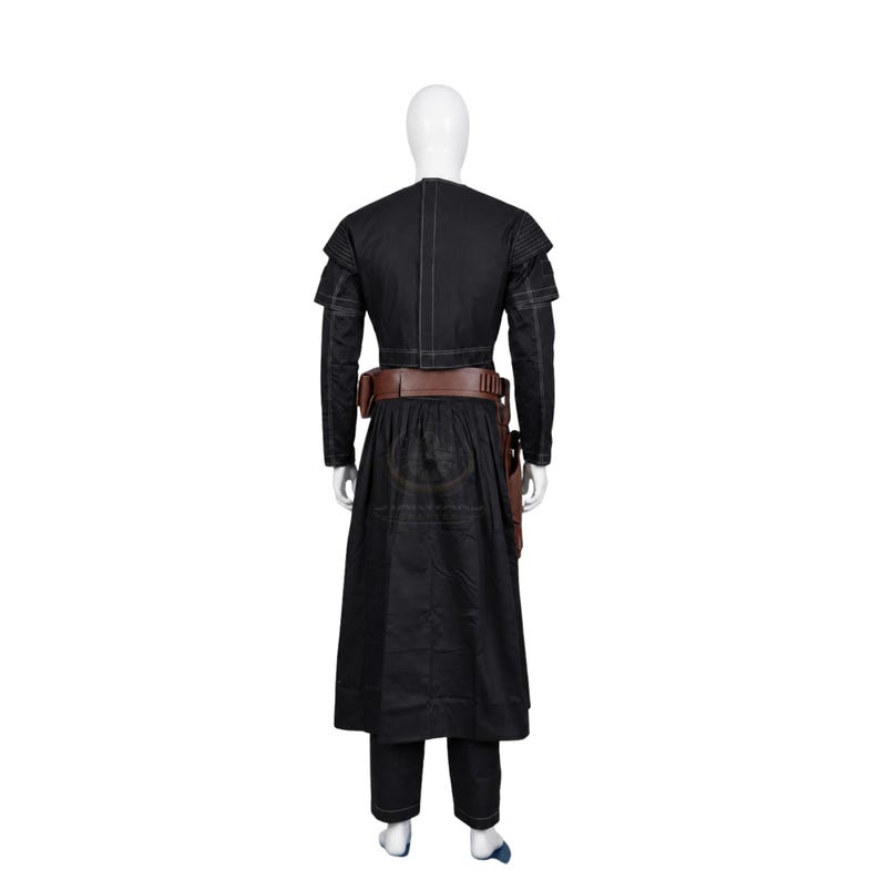Puede incluir: Una chaqueta negra de manga larga con hombros estructurados y costuras blancas, combinada con una falda negra larga hasta el suelo y pantalones. Un cintur&oacute;n ancho de cuero marr&oacute;n con una funda y trabillas para munici&oacute;n se lleva en la cintura.
