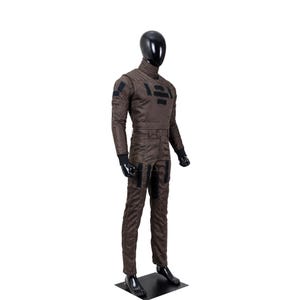 May include: A dark brown long-sleeved jumpsuit worn by a black mannequin. The garment features a high collar, black rectangular patches on the chest, shoulders, and thighs, and black ribbed cuffs at the wrists. The fabric has visible stitching.