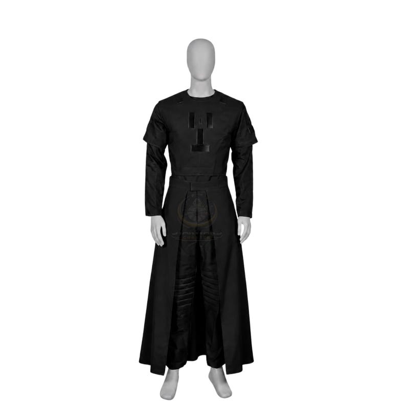 Pode incluir: Um conjunto de traje preto composto por uma blusa de manga curta com um emblema geom&eacute;trico no peito, combinado com cal&ccedil;as a condizer e uma saia comprida aberta &agrave; frente. O conjunto apresenta uma cor escura uniforme e design estruturado.