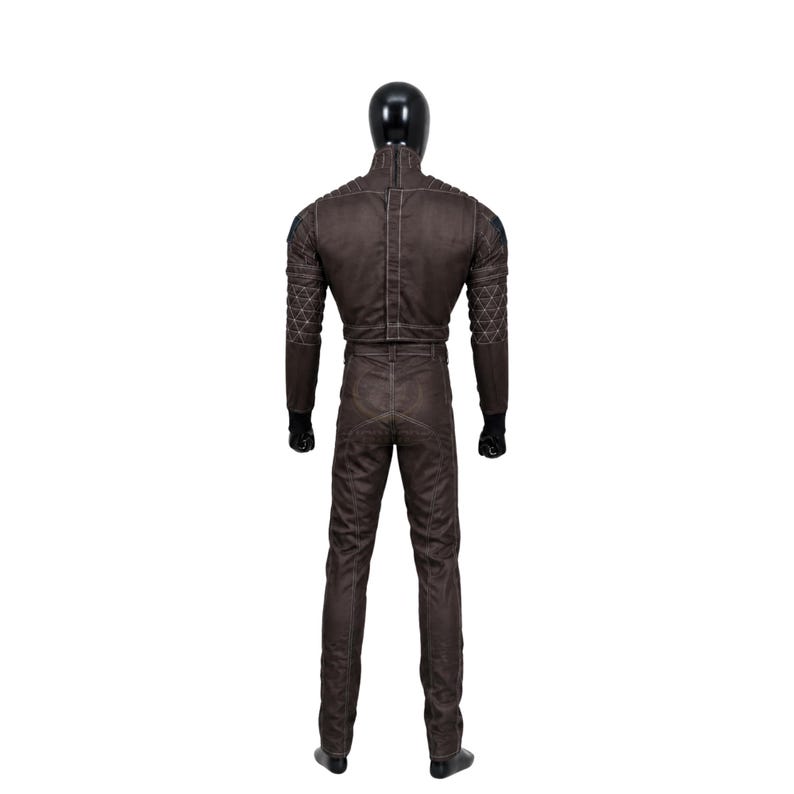 May include: A dark brown full-body jumpsuit worn by a black mannequin, featuring a high collar, long sleeves with quilted geometric patterns on the shoulders and forearms, a central vertical zipper, and visible stitching throughout the garment.