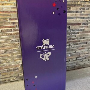 May include: A purple box with the Stanley logo and the letters "OK" in white. The box has a glossy finish and is decorated with red, black, and white stars. The box is rectangular and stands upright.