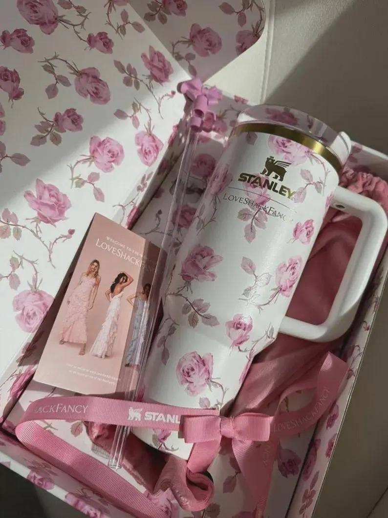 May include: A white Stanley tumbler with a pink rose pattern, inside a gift box with matching floral design. The box includes a pink ribbon, a card with images of dresses, and the text "LOVESHACKFANCY".