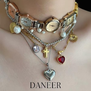 May include: A unique necklace featuring a watch band base with multiple watch faces, pearls, and various charms. Charms include a heart, cross, and sunburst. The text "DANEER" and "Grand Goose's original design" are visible.