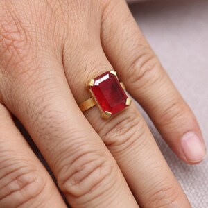 Peut inclure: Une bague en or orn&eacute;e d'une grande pierre pr&eacute;cieuse rouge fonc&eacute; de forme rectangulaire. Le sertissage de la bague est simple et &eacute;l&eacute;gant, la pierre pr&eacute;cieuse &eacute;tant le point central. La bague est port&eacute;e sur une main.