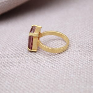 Peut inclure: Une bague en or avec une pierre pr&eacute;cieuse rose rectangulaire. La monture et le sertissage de la bague sont en or mat. La pierre est rose clair et sertie dans une lunette rectangulaire.