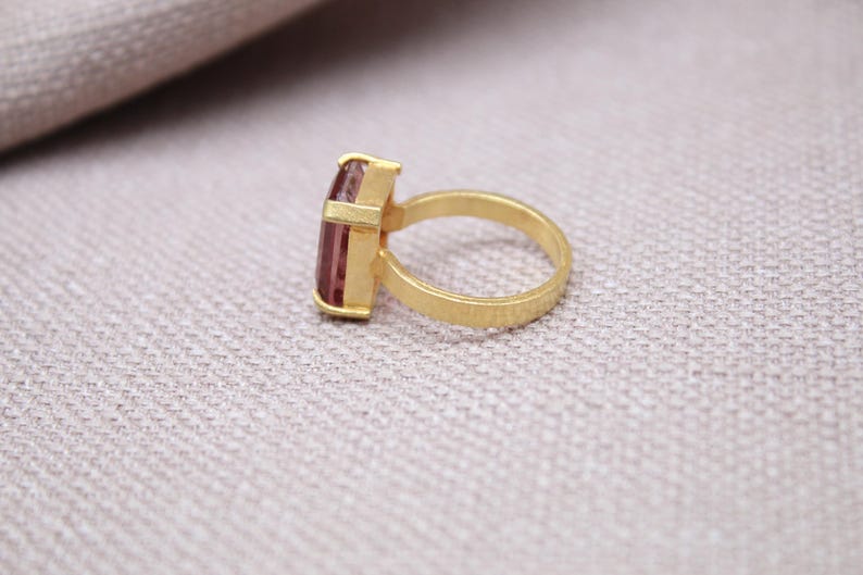 Peut inclure: Une bague en or avec une pierre pr&eacute;cieuse rose rectangulaire. La monture et le sertissage de la bague sont en or mat. La pierre est rose clair et sertie dans une lunette rectangulaire.