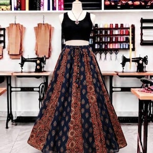 Puede incluir: Un top corto negro sin mangas combinado con una falda larga de cintura alta con un intrincado estampado de cachemira en azul oscuro y color óxido. La falda tiene una cintura con cordón y una silueta acampanada sobre un maniquí.