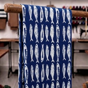 May include: A deep blue fabric featuring a repeating pattern of white fish illustrations. The fish are arranged in vertical rows, each depicted with detailed line work. The background of the fabric has a subtle, tiny white dot texture.