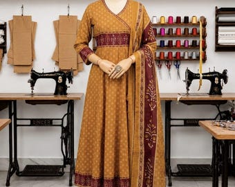 May include: A mustard yellow A-line dress with a V-neckline, three-quarter sleeves, and a dark maroon band featuring a white floral print at the waist and hem. The dress is paired with matching trousers, a long shawl, and beige pointed-toe flats.