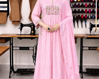 May include: A light pink A-line kurta dress featuring a round neckline with a small slit, three-quarter sleeves, and delicate floral embroidery on the chest and cuffs. The outfit includes matching straight-leg trousers and a long, sheer dupatta.