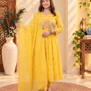 Puede incluir: Un vestido amarillo brillante de manga larga con corte en A, que presenta un escote con abertura y bordados florales intrincados en rosa, verde y blanco en el corpiño y los puños. El vestido incluye un dupatta amarillo a juego con detalles florales.