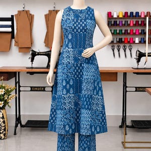 Puede incluir: Un conjunto de túnica azul sin mangas y pantalones anchos a juego con un diseño de patchwork de varios patrones geométricos y florales estampados en blanco. El conjunto se muestra en un maniquí en un estudio de costura con telas.