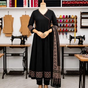 May include: A black long-sleeved dress with a V-neckline, featuring intricate copper-colored geometric embroidery along the neckline, cuffs, and hem. The dress is paired with a matching black dupatta with a decorative border and black trousers.