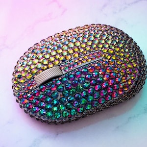 May include: A computer mouse encrusted with iridescent rhinestones in a rainbow of colours. The scroll wheel and buttons are visible. The rhinestones shift from yellow to green to blue. The mouse sits on a white and pink marble surface.