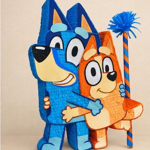 Peut inclure: Une piñata en forme de chien bleu et orange représentant deux personnages de dessin animé qui s'enlacent. Le grand personnage bleu se tient derrière le petit personnage orange. Un bâton rayé bleu et orange avec une frange bleue est à côté.