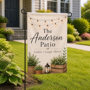 May include: A cream-colored garden flag featuring a string of glowing lights at the top, the text "The Anderson Patio" in black, and "Gather • Laugh • Relax" below. The design includes illustrations of potted plants and a lantern.