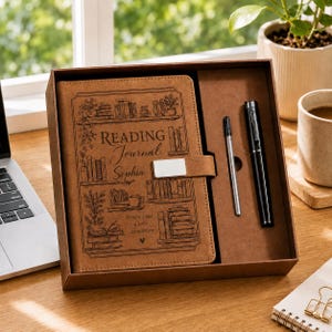 May include: A tan leather-like reading journal with a metal clasp, featuring engraved illustrations of bookshelves and the text Reading Journal Sophia Every page a new adventure, presented in a box with a black pen and a silver metal refill.