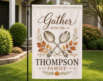 May include: A rectangular garden flag featuring the text Gather WITH THE THOMPSON FAMILY. The design includes a crossed spoon and salad fork illustration surrounded by autumn leaves in shades of orange, yellow, and brown, with a small orange pumpkin.