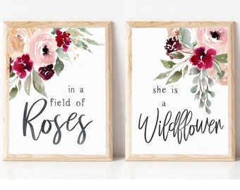 May include: Two framed prints with watercolor floral designs. The left print features a pink and burgundy floral arrangement with the text "in a field of Roses". The right print features a similar floral arrangement with the text "she is a Wildflower".