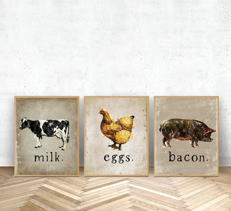 Puede incluir: Conjunto de tres l&aacute;minas enmarcadas con acuarelas de animales de granja. Las l&aacute;minas incluyen una vaca en blanco y negro con la palabra "milk", una gallina marr&oacute;n con "eggs" y un cerdo oscuro con "bacon". Estilo r&uacute;stico y vintage.