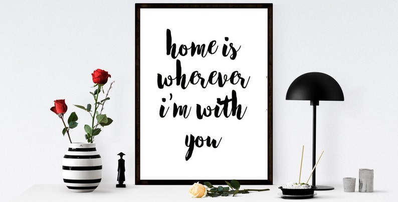 May include: A framed print with the text "home is wherever I'm with you" in black script. A black and white striped vase holds red roses. A black lamp and decorative items complete the scene.