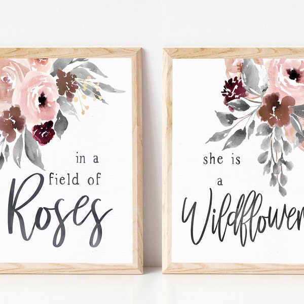 Pode incluir: Duas impressões emolduradas com desenhos florais em aquarela. A impressão da esquerda apresenta um buquê de flores rosa, bordô e cinza com o texto "in a field of Roses". A impressão da direita apresenta um buquê de flores rosa, bordô e cinza com o texto "she is a Wildflower".