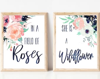 May include: Two framed prints with floral designs and text. The left print features a watercolor floral design with pink, white, and blue flowers and the text "In a field of roses". The right print features a watercolor floral design with white, pink, and green flowers and the text "She is a wildflower".