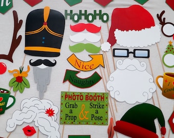 May include: A collection of Christmas-themed photo booth props. Includes a Santa hat, elf hat, mustaches, glasses, and signs that say "Nice," "Naughty," and "Photo Booth: Grab a Prop & Strike a Pose."