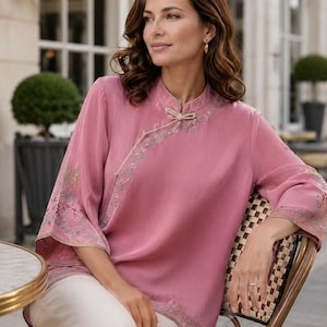 May include: A dusty rose blouse featuring a mandarin collar, a diagonal front closure with a decorative knot button, and three-quarter length sleeves. The garment is adorned with intricate floral embroidery along the neckline, cuffs, and hem.