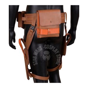 May include: A brown leather utility belt with multiple pouches and a holster. The belt features a large central pouch with an orange accent and a smaller pouch on the left side. The belt is designed to be worn around the waist and thighs.