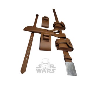 Op de afbeelding: Bruine leren utility riem met meerdere zakjes, riemen en een zilveren gesp. De riem heeft een reeks bevestigde zakjes en riemen, ontworpen voor het dragen van diverse items. Het Star Wars-logo is zichtbaar.
