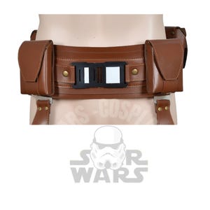 May include: A brown leather belt with two pouches and a central buckle. The belt has a rectangular black and white buckle and is secured with suspender-style straps. The belt is designed to be worn around the waist.