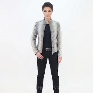 May include: A long-sleeved jacket featuring a grey and white snakeskin pattern with a mandarin collar and a front zipper closure. The jacket is worn over a solid black t-shirt and black trousers with a black belt featuring a silver-toned buckle.