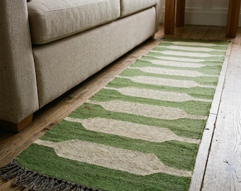 Puede incluir: Una alfombra de pasillo rectangular con un patrón geométrico repetitivo en verde salvia y blanco roto. La alfombra tiene un tejido texturizado y está rematada con flecos cortos de color gris oscuro en los dos extremos más cortos.