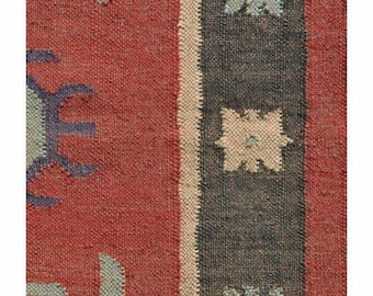 Puede incluir: Una alfombra textil tejida con un fondo rojo intenso y patrones geométricos azul claro. Un borde gris oscuro recorre verticalmente, decorado con una fila repetitiva de pequeños motivos en forma de estrella claros separados por una fina franja beige.