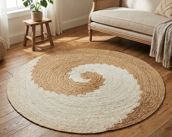 Puede incluir: Una alfombra redonda con un patrón de espiral de fibras trenzadas en color tostado natural y blanco roto. La alfombra está fabricada con material trenzado y se extiende sobre un suelo de madera, mostrando un diseño circular bicolor.