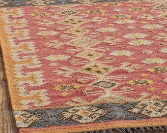 Puede incluir: Una alfombra rectangular con una base de color rojo vibrante y patrones geométricos intrincados en amarillo, azul y crema. La alfombra tiene un borde ancho con motivos de diamantes repetidos y flecos en los lados cortos del tejido.