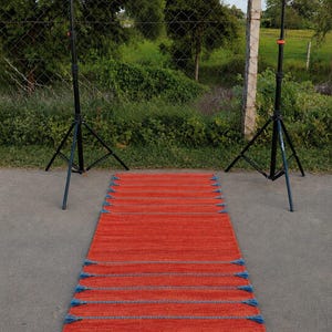 May include: A rectangular runner rug featuring a vibrant orange base color with horizontal rows of textured blue stitching. The rug is accented with small blue tassels attached at regular intervals along both long edges of the woven fabric.