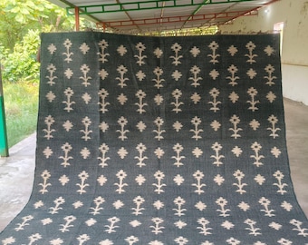 Puede incluir: Una alfombra rectangular grande de color gris carbón profundo con un patrón repetitivo de motivos florales estilizados y pequeñas formas de diamante en color blanco roto. La alfombra tiene un tejido texturizado y flecos cortos.